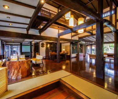 Spacious wooden ryokan lounge with exposed beams, tatami step and garden view at Shirakabe Shizuoka
