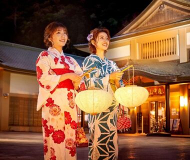 Two guests in yukata holding lanterns outside Shirasagiyu Tawaraya entrance in Ishikawa
