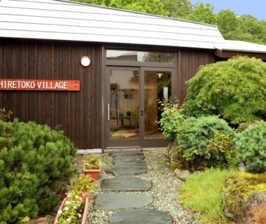 Stepping stone path to wooden ryokan entrance with shrubs and Shiretoko Village sign in Hokkaido