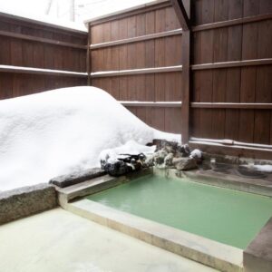 Outdoor stone onsen with pale green water, wooden fence and snow piled on surrounding bench at Shiunso, Tochigi