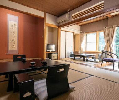 Spacious tatami room with low table, zabuton chairs, alcove scroll and balcony overlooking greenery at Shiunso, Kanagawa