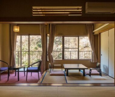 Tatami room with low table, chairs and balcony overlooking trees at Shiunso in Kanagawa