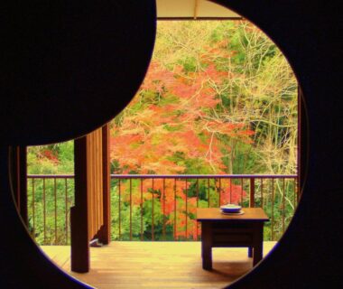 Circular window framing autumn maple trees, wooden veranda and low table at Shiunso ryokan in Kanagawa, Kantō