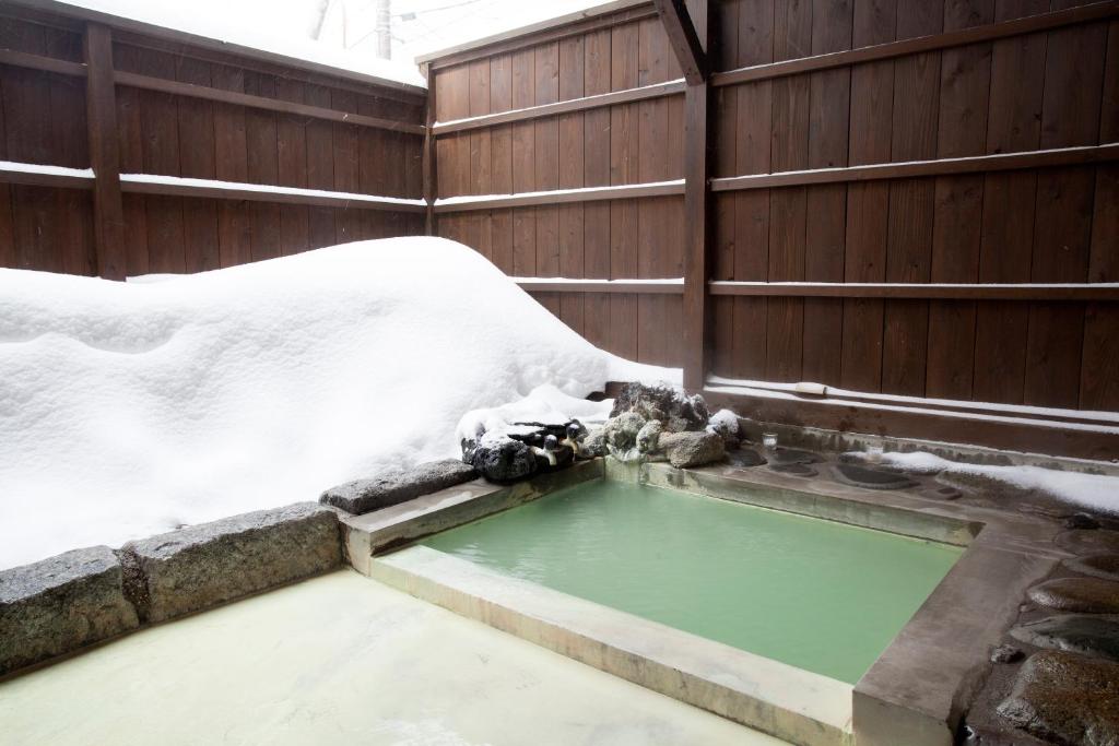 Snowy outdoor onsen at Shiunso, Tochigi Outdoor stone onsen with pale green water, wooden fence and snow piled on surrounding bench at Shiunso, Tochigi