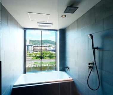 Bathtub and shower with large window facing river and hillside at Shizuru 鴨川 Kyoto