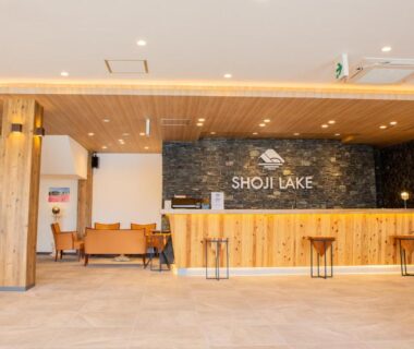 Warm wood reception counter with seating and stone wall signage at Shoji Lake Hotel in Yamanashi