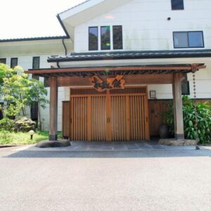 Wooden slatted entrance doors and covered porch at Shokinkan ryokan with shrub landscaping Kumamoto Kyūshū