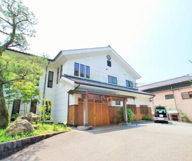 White two-story ryokan exterior with wooden entrance doors, courtyard trees and driveway in Kumamoto, Kyushu