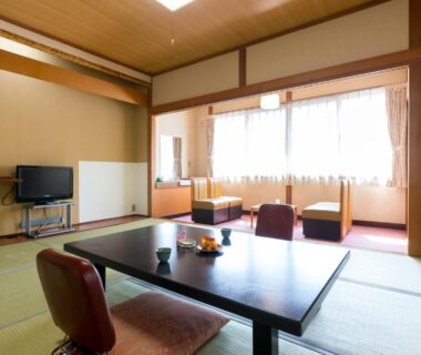 Spacious tatami room with low table, floor chairs, TV and window seating at Shosenkaku in Nagano