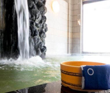 Indoor onsen bath with rock waterfall feature and wooden bucket at Shosenkaku, Nagano