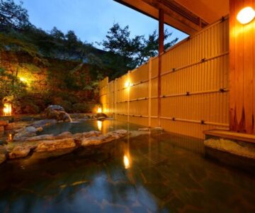 Outdoor onsen bath with wooden fence, stone edging and evening lanterns at Shouhakutei Azumaso, Yamagata