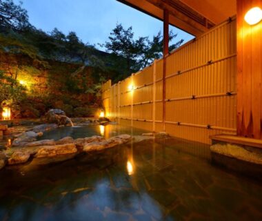 Outdoor onsen bath with wooden fence, stone edging and evening lanterns at Shouhakutei Azumaso, Yamagata