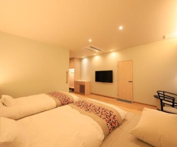 Twin low futon beds on tatami floor with wall TV and seating in Shouhakutei Azumaso guest room, Yamagata