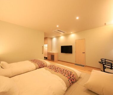 Twin low futon beds on tatami floor with wall TV and seating in Shouhakutei Azumaso guest room, Yamagata