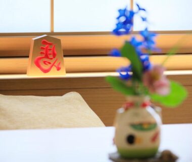 Small ceramic vase with blue flowers on low table, cushion and wooden window ledge in ryokan room Yamagata