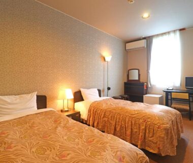 Twin beds with patterned bedspreads, bedside lamps and desk at Shugyoku no Yu Yakushido Onsen in Iwate