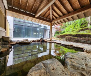 Rock-edged covered onsen with timber roof, glass wall and tiered garden at Shugyoku no Yu in Iwate