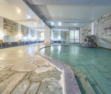 Spacious indoor onsen bath with stone flooring and washing stations at Shuzenji Onsen Hotel Takitei, Shizuoka