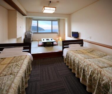 Room with twin beds, raised tatami seating area and wide window overlooking water at Simamegurinoyado Sakai, Miyagi