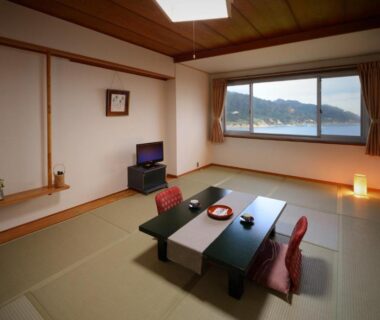Tatami room with low table, floor cushions, tokonoma alcove and large window overlooking coastal scenery in Miyagi