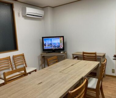 Long wooden table with chairs, TV and air conditioner in communal room at Sky Tree INN II Tokyo