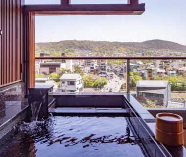 Stone indoor bath with wooden bucket and city and mountain view at Sora Niwa Terrace Kyoto Bettei, Kyoto
