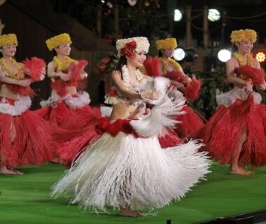Hawaiian dancers in red and white grass skirts performing on stage at Spa Resort Hawaiians Monolith Tower, Fukushima