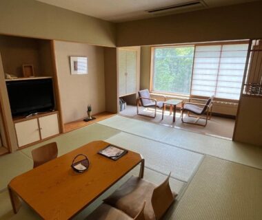 Tatami room with low table, zabuton cushions, shoji screens and window greenery at Suichokan Hokkaidō