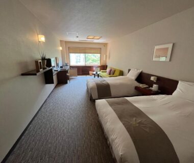 Spacious twin bedroom with two beds, seating area, desk and large window overlooking greenery