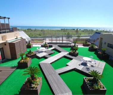 Rooftop terrace with wooden walkways, planter beds, lounge seating and distant coastal view at Spa&Resort Kujukuri in Chiba