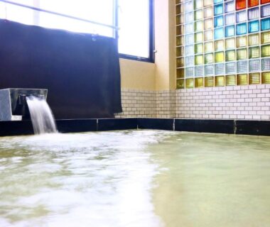 Indoor tiled bath with flowing spout and glass block window at Sports Plaza Shiki Haradaso Niigata