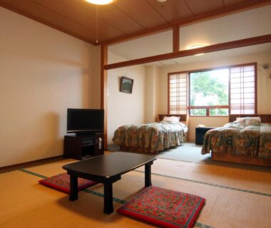 Tatami room with low table, zabuton cushions, two beds and shoji window overlooking greenery at Star Hotel Akakura Niigata