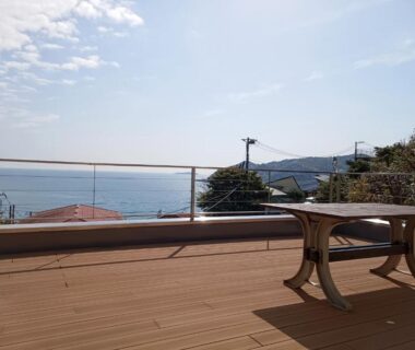 Wooden deck terrace with railing and table overlooking the ocean and coastline at StellaMarina ATAMI, Shizuoka, Japan