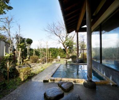 Stone outdoor onsen beside glass wall and traditional garden at Suehirokan, Niigata, Chūbu