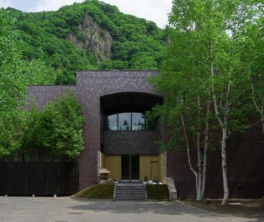 Brick façade of Suigan ryokan with arched window, stone steps and birch trees by forested hillside in Hokkaidō