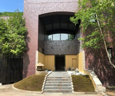 Front stone steps leading to Suigan wooden entrance doors framed by trees and mossy landscaping in Hokkaidō