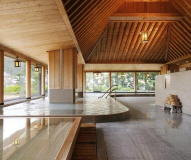 Spacious indoor onsen with wooden beams, stone floor and large windows overlooking garden at Suimeikan, Gifu, Chūbu
