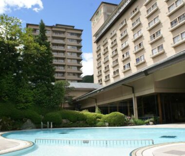 Outdoor swimming pool beside multi-story ryokan buildings and landscaped garden at Suimeikan in Gifu