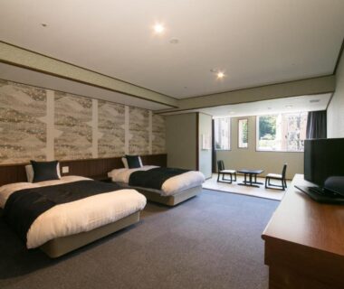 Spacious room with three low beds, seating area by window and decorative wall panels at Suimeikan, Gifu