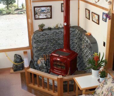 Cozy seating with floral cushions, red wood stove and tiled hearth beside a large window at Suisensou