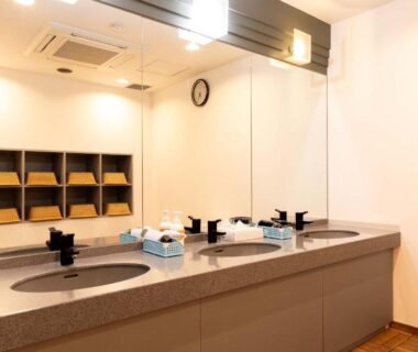 Shared sink area with multiple basins, large mirror, toiletries and wooden cubby shelves at Suizansou in Hyōgo
