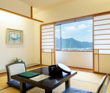 Traditional tatami room with low table, shoji screens and mountain view through large window at Suizansou in Hyōgo Kansai