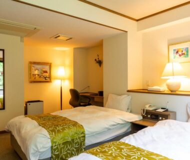 Twin beds and seating area with greenery visible through window at Suizansou Hyōgo Kansai
