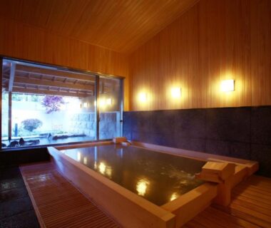 Indoor wooden onsen tub with warm lighting and garden view at Suizantei Club Jozankei in Hokkaidō