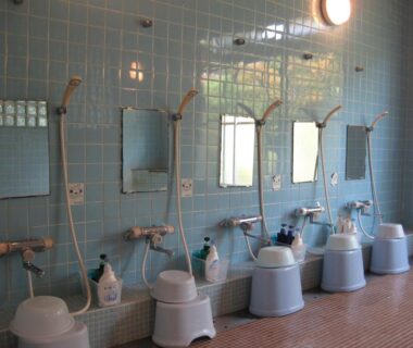 Row of stools and handheld showers in a tiled communal bathing area at Suminoe Ryokan Hiroshima