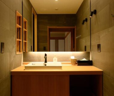 Wooden vanity with sink, backlit mirror and tiled walls in Suminoyu ryokan bathroom, Nagano