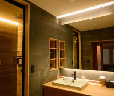 Sink with illuminated mirror, wooden counter and tiled walls in Suminoyu bathroom, Nagano