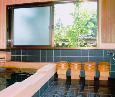 Tiled indoor onsen with wooden soaking tub, stools and buckets beside a garden-facing window at Sumiyoshi Ryokan
