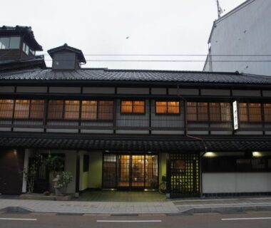 Two-story traditional wooden facade with lit shoji windows and street-level entrance at Sumiyoshiya in Ishikawa