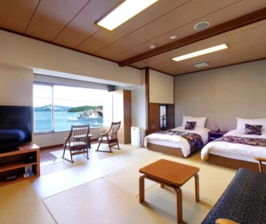 Tatami-floored room with twin beds, low table, sofa and coastal view at Sun Urashima Yuki no Sato Mie